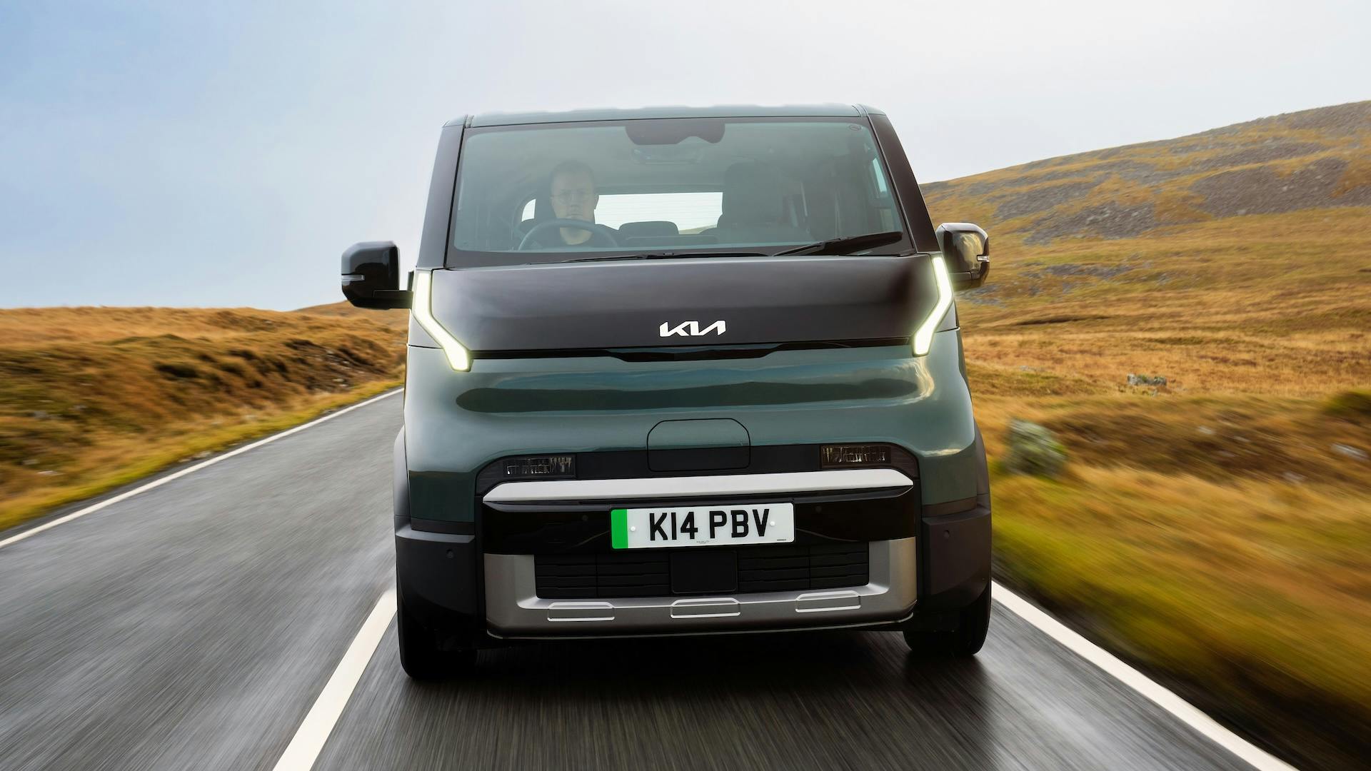 Green 2025 Kia PV5 Passenger driving on a country road, front.